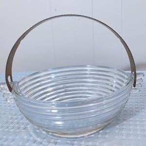 May include: A clear glass bowl with a silver metal handle. The bowl has a ribbed design and is perfect for serving fruit or snacks.