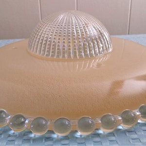 May include: A vintage light fixture with a frosted, peach-colored shade and a clear, textured dome. The shade is edged with clear, round glass beads. This ceiling light fixture is a classic design.
