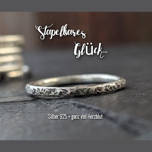 Könnte beinhalten: Ein silberner Ring mit einer strukturierten, gehämmerten Oberfläche. Der Ring ist stapelbar und trägt die Aufschrift "Stapelbares Glück... Silber 925 + ganz viel Herzblut".