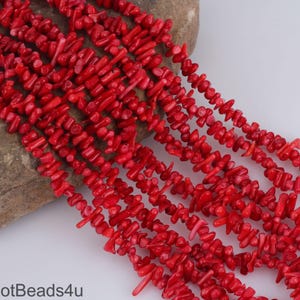 May include: A strand of red coral beads, each bead is a small, irregular piece of coral. The beads are strung together to form a long necklace.