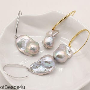 May include: A pair of hoop earrings with large, irregular, white baroque pearls hanging from them. The hoops are made of silver and gold metal.