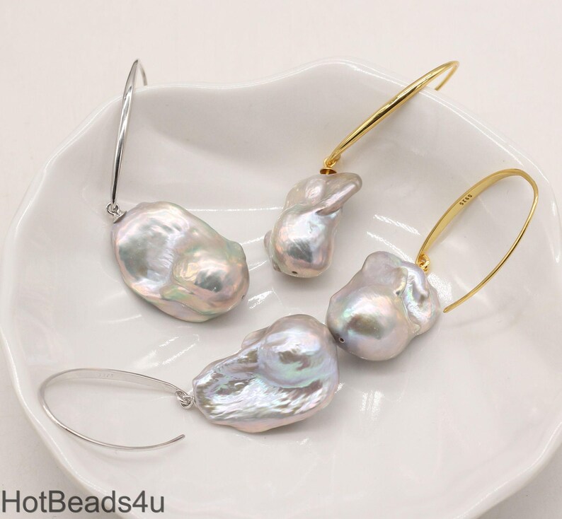 May include: A pair of hoop earrings with large, irregular, white baroque pearls hanging from them. The hoops are made of silver and gold metal.
