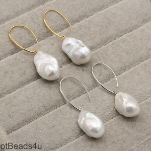 May include: A pair of earrings with large, white, baroque pearls hanging from gold and silver hoops.
