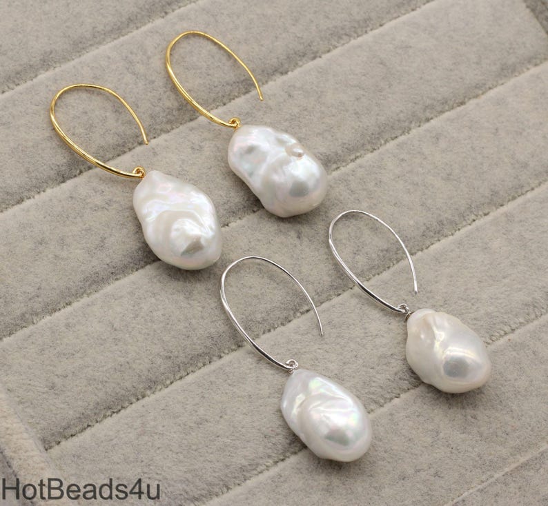 May include: A pair of earrings with large, white, baroque pearls hanging from gold and silver hoops.