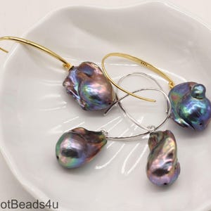 May include: A pair of earrings featuring iridescent baroque pearls with gold and silver hoops. The pearls are a deep purple and green color.
