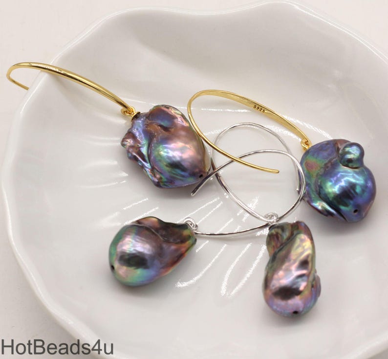 May include: A pair of earrings featuring iridescent baroque pearls with gold and silver hoops. The pearls are a deep purple and green color.