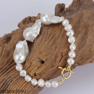 May include: A white pearl bracelet with a gold toggle clasp. The bracelet features three large, irregular shaped pearls and smaller round pearls.