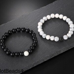 May include: Two beaded bracelets, one black and one white with a black lava bead. The black bracelet has a single white bead.