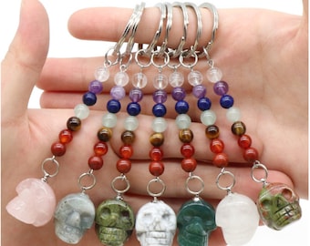 May include: Seven colorful crystal skull keychains with a rainbow of beads. The beads are clear, amethyst, lapis lazuli, green aventurine, tiger's eye, and red jasper.