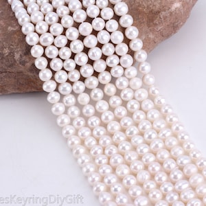 Puede incluir: Una hebra de perlas de agua dulce blancas, cada perla es redonda y lisa. Las perlas están enhebradas en un hilo blanco y tienen un diámetro aproximado de 6 mm.