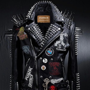 Puede incluir: Chaqueta de cuero negro con tachuelas y parches plateados. La chaqueta tiene cierre de cremallera y varios bolsillos. Los parches incluyen "Punk Rock", "Cannibal Corpse", "The Glamour Corpse" y "The Forest".