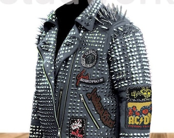 Pode incluir: Uma jaqueta de couro preta com tachas e espinhos prateados. A jaqueta tem vários patches costurados, incluindo um patch que diz "Addiction" e um patch com uma caveira e ossos cruzados. A jaqueta está sobre uma superfície de madeira.