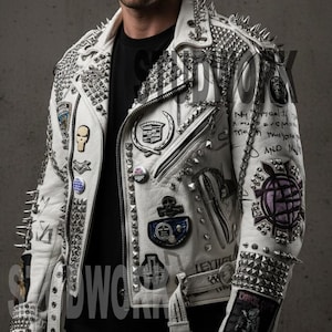 May include: White leather jacket adorned with silver spikes and studs. The jacket has various patches, zips, and a belt. The design includes a skull, Cadillac logo, and handwritten text. It is worn over a black top.