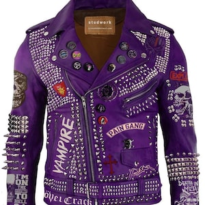 Op de afbeelding: Paarse leren jas met zilveren studs, spikes en patches. Met de tekst "VAMPIRE", "PAIN GANG" en schedelafbeeldingen. Voorzien van een ritssluiting. Een opvallend kledingstuk.