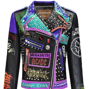 May include: Black leather jacket with colorful patches and silver studs. Features band logos like AC/DC and Megadeth, along with the text "Leftover Crack" and "Oxymoron". The jacket has a purple zipper and accents, with a studded collar.
