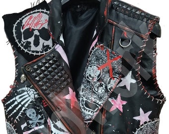 Könnte beinhalten: Schwarze Lederweste mit Punk-Rock-Ästhetik. Sie zeigt mehrere Schädelmotive, rote und rosa Farbschleier und einen Patch mit der Aufschrift "Vampire".