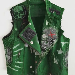 May include: Green leather vest with skull and crossbones graphics, studs, and a zipper closure. The vest features a distressed design with white accents and a skull patch on the back. The vest is hanging on a white hanger.