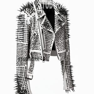 May include: White leather biker jacket, heavily embellished with black spikes and studs. The jacket has a notched collar, an asymmetrical zip, and multiple pockets. The sleeves and shoulders are adorned with long, pointed spikes.