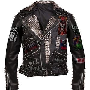 May include: Black leather jacket adorned with silver studs and spikes. The jacket displays various patches with graphic designs and text, including "Loud Pipes Save Lives Because" and "The Exploited". It has a zip closure and a belt.
