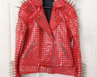 Puede incluir: Chaqueta de cuero roja con púas y tachuelas plateadas. La chaqueta tiene un estilo motero clásico con cuello de solapa, cierre de cremallera y múltiples bolsillos. Las mangas y el cuello están adornados con largas púas plateadas.