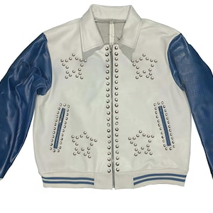 May include: White jacket with blue sleeves. The jacket features star-shaped stud embellishments and a zip closure. The cuffs and hem have blue and white striped detailing. A classic bomber jacket style.