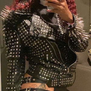 May include: Black leather jacket with silver studs and spikes. The jacket features a zipper closure and a belted waist. The shoulders are adorned with long, silver spikes. A bold and edgy fashion statement.