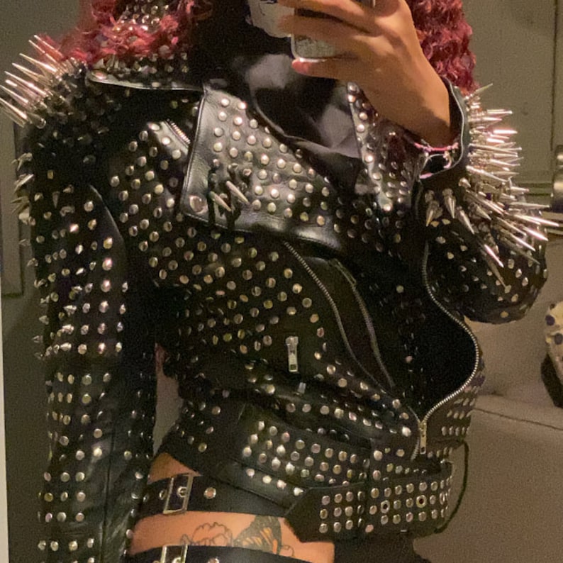 May include: Black leather jacket with silver studs and spikes. The jacket features a zipper closure and a belted waist. The shoulders are adorned with long, silver spikes. A bold and edgy fashion statement.