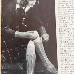 May include: Black and white image of a woman wearing a knitted hat, mittens, and knee-high socks. The socks and mittens have a cable stitch design. The woman is wearing a dark jacket and a plaid skirt. The image is from a vintage knitting pattern.