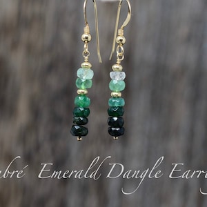 May include: A pair of ombre emerald dangle earrings with gold hooks and a graduated color scheme from light green to dark green.