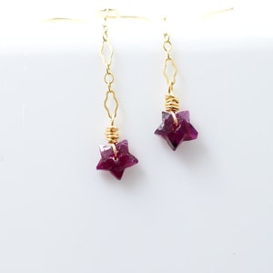 May include: A pair of gold dangle earrings with star-shaped purple gemstones.