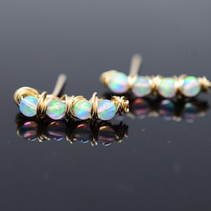 May include: A pair of gold wire earrings with iridescent opal beads. The earrings are curved and have a minimalist design.