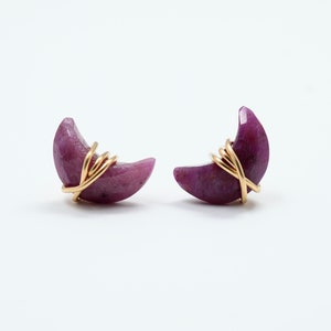 May include: A pair of crescent moon shaped earrings made with purple gemstone and gold wire.
