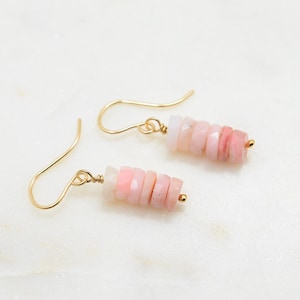 May include: A pair of gold earrings with pink opal stones. The earrings are made of gold wire and have a simple design. The pink opal stones are stacked on top of each other and are a light pink color.