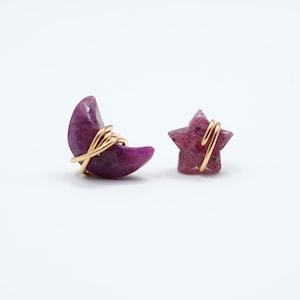 May include: A pair of earrings featuring a crescent moon and a star shape, both made of pink stone and wrapped in gold wire.