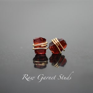 May include: A pair of raw garnet stud earrings with gold wire wrapping. The garnet stones are a deep red color and have a natural, rough texture.