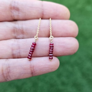 May include: A pair of gold dangle earrings with a chain and a line of red ruby beads.