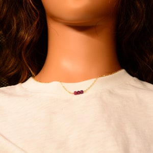May include: A gold chain necklace with three small, dark purple beads.