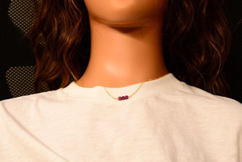 May include: A gold chain necklace with three small, dark purple beads.
