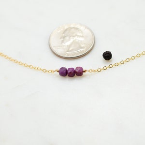 May include: A delicate gold chain necklace with three small purple gemstone beads.