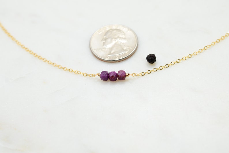 May include: A delicate gold chain necklace with three small purple gemstone beads.