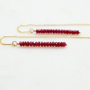 May include: A pair of gold earrings with a long chain and a line of red ruby beads.