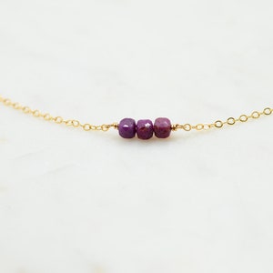 May include: A delicate gold chain necklace with three small purple gemstone beads.