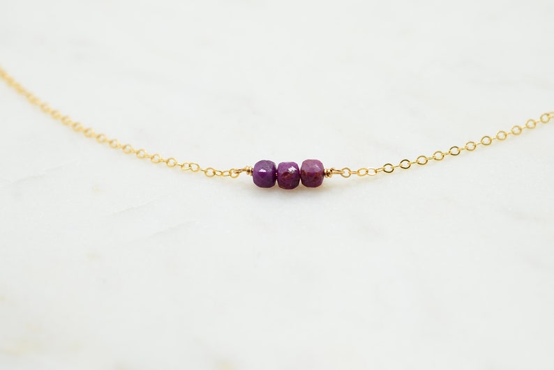 May include: A delicate gold chain necklace with three small purple gemstone beads.