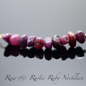 May include: A delicate gold chain necklace with a row of raw, rustic ruby gemstones. The rubies are a mix of pink and purple hues.