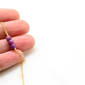 May include: A delicate gold chain necklace with three small, faceted purple gemstones.