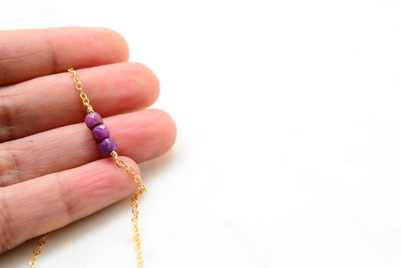 May include: A delicate gold chain necklace with three small, faceted purple gemstones.