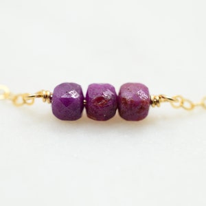 May include: A delicate gold chain necklace with three faceted purple gemstone beads.