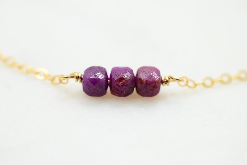 May include: A delicate gold chain necklace with three faceted purple gemstone beads.