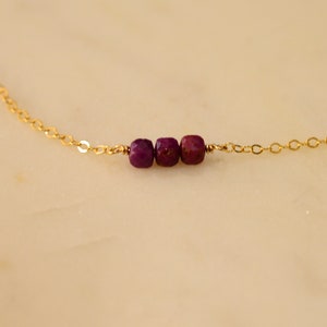 May include: A delicate gold chain necklace with three small, faceted, purple gemstones.