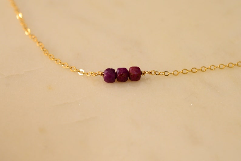 May include: A delicate gold chain necklace with three small, faceted, purple gemstones.